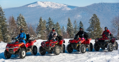 Group of people on off road vehicles in the winter with a mountain in the background.