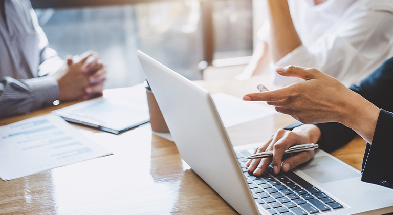 Two people meeting with coffee, papers, and a laptop