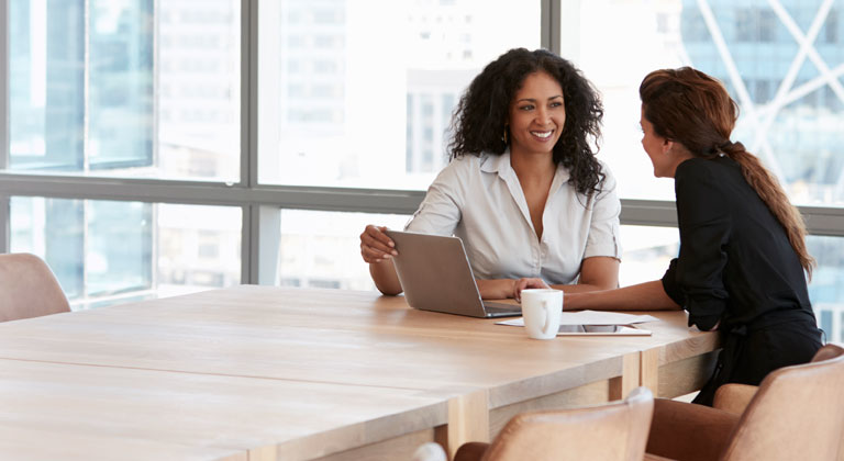 Two women in meeting smiling with laptop on table