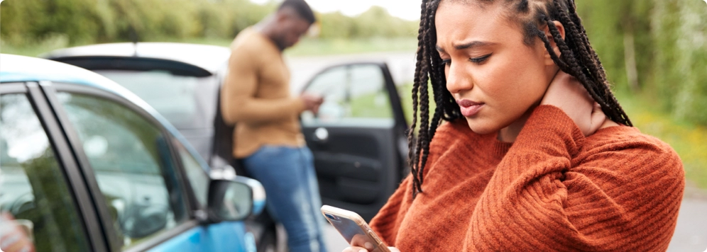 woman with cell phone after car wreck holding her neck