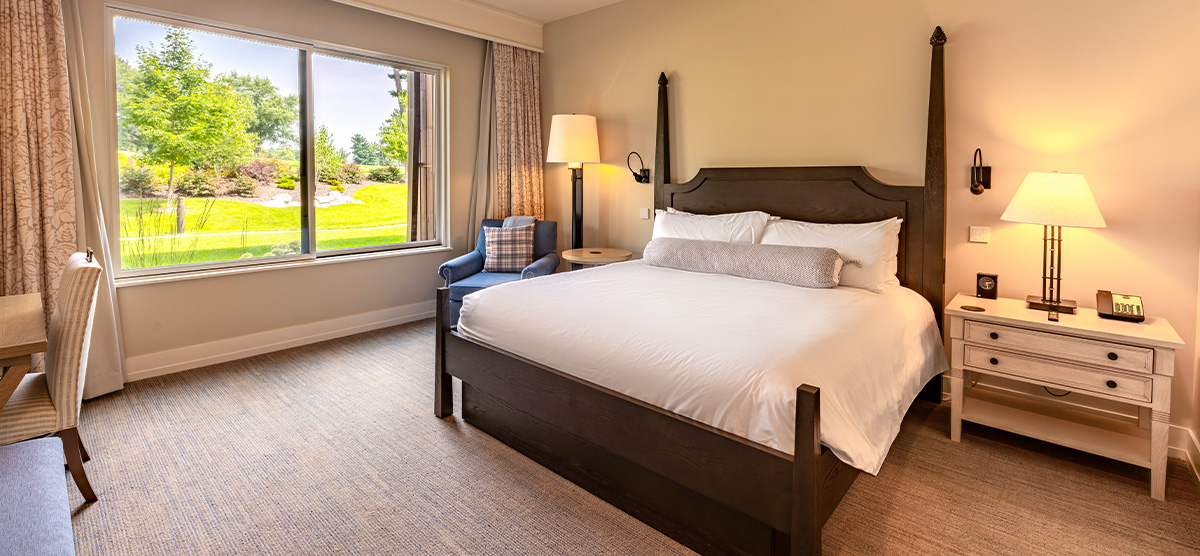 carousel-accessible-golf-view-king-suite-1-1200x556 Room with a king sized bed, large window, and desk area.