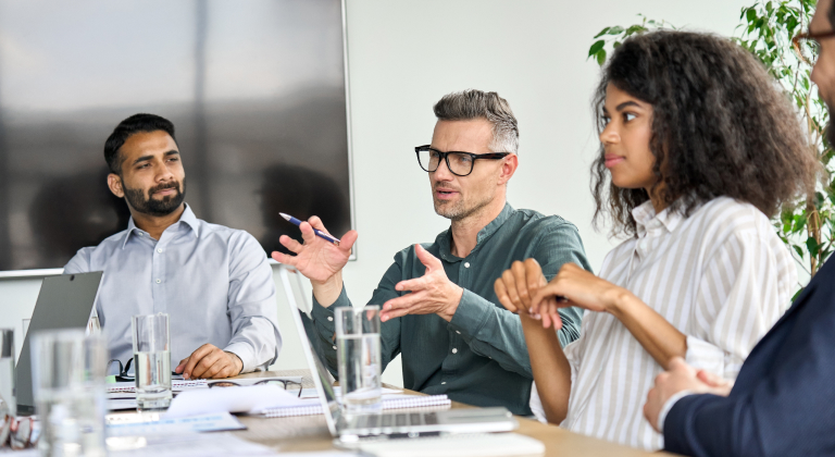 Diverse group of professionals in a meeting, with one man speaking and gesturing.