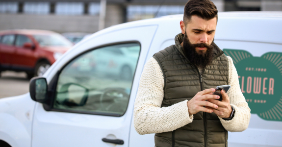 Man with a beard using a smartphone in front of a white delivery van