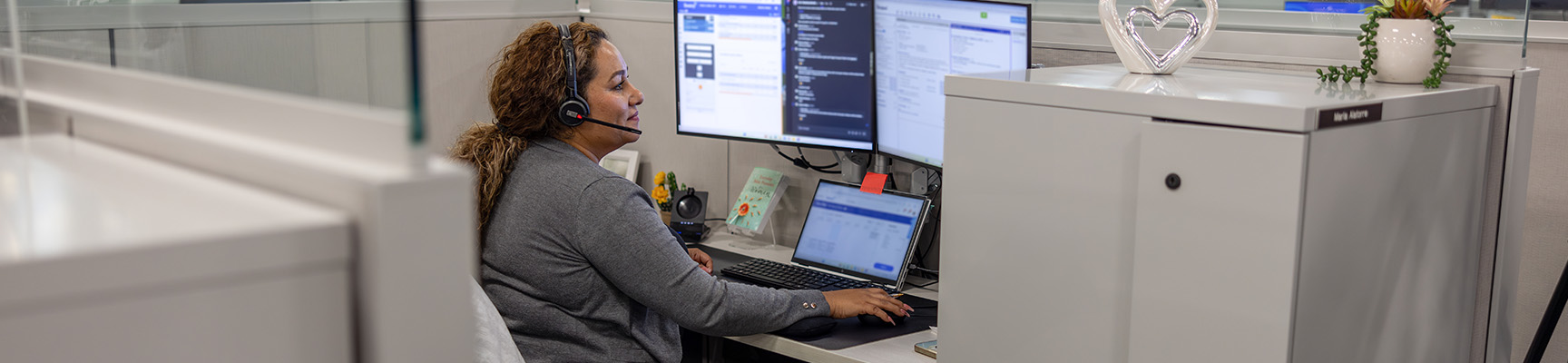 Woman talking with a customer through a headset while working on a computer.