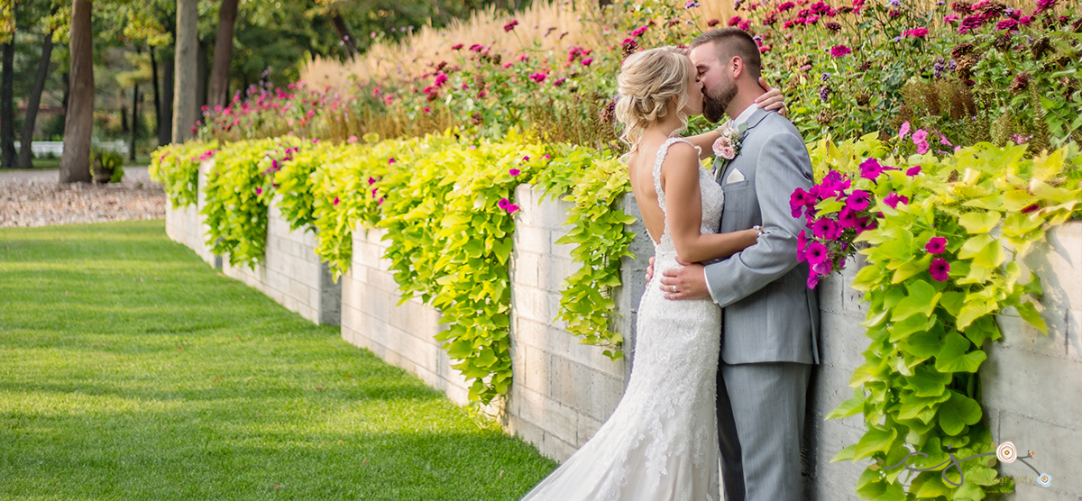 Bride and groom kissing by greenery in the front of SentryWorld