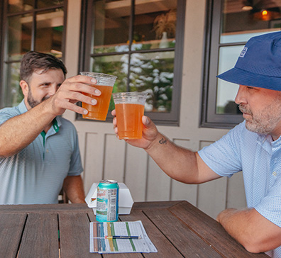 Two men drinking glasses of beer outside a refreshment station while golfing at SentryWorld.