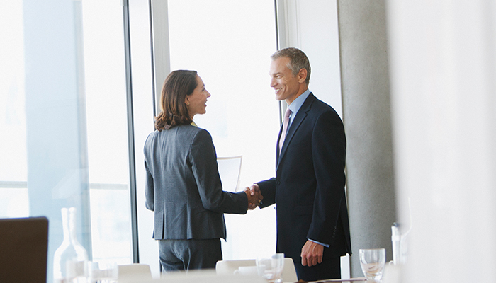 Two business professionals shaking hands in a modern office.