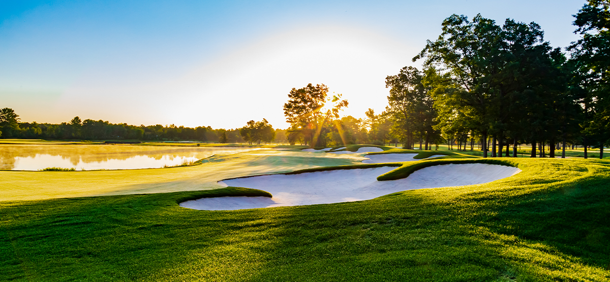 Sunshine peaking through trees onto a SentryWorld putting green with sand traps