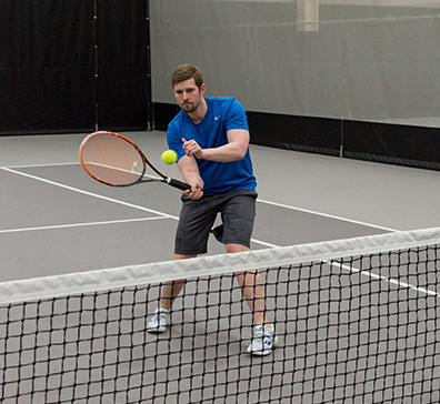 Player hitting a tennis ball on a court in the SentryWorld fieldhouse