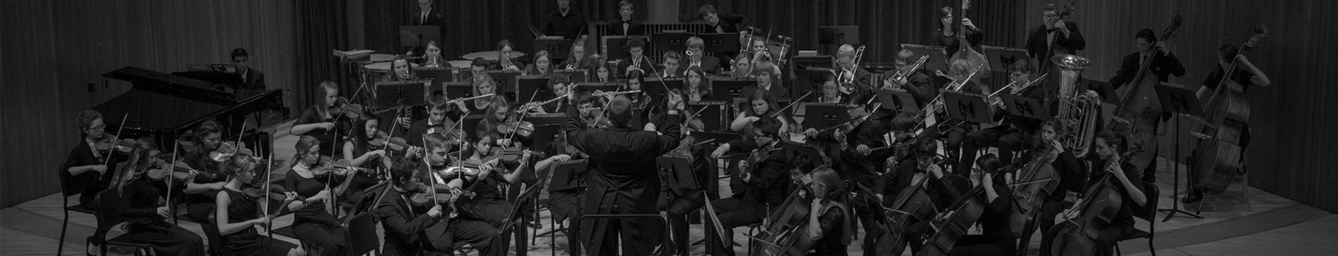 Black and white image of a youth orchestra playing on stage. 