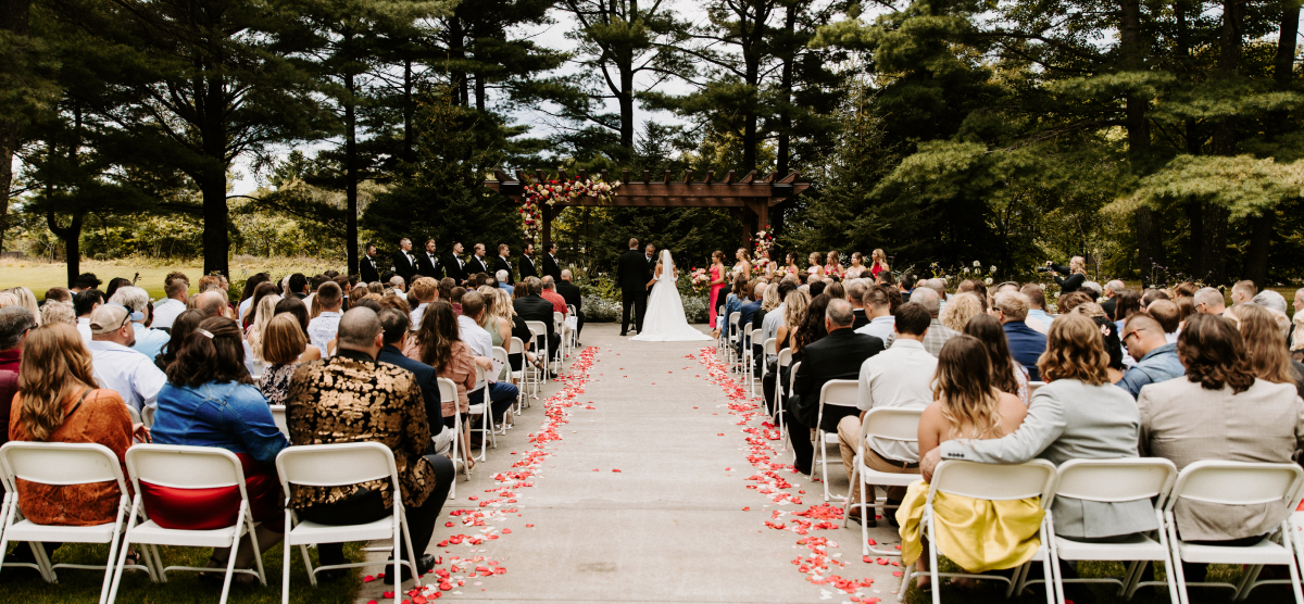 Guests seated at an outdoor wedding ceremony, watching the bride and groom at the altar.