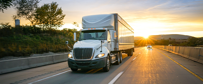 Semi trailer truck driving down highway at sunset