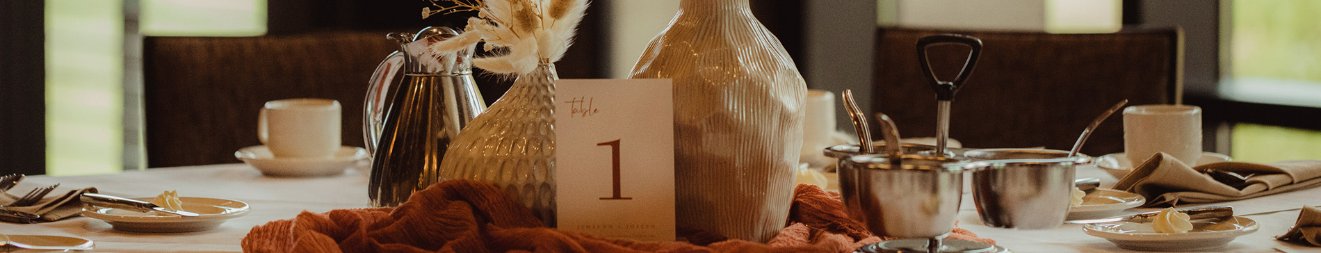 Two vases filled with feathers and a table number card for a wedding reception