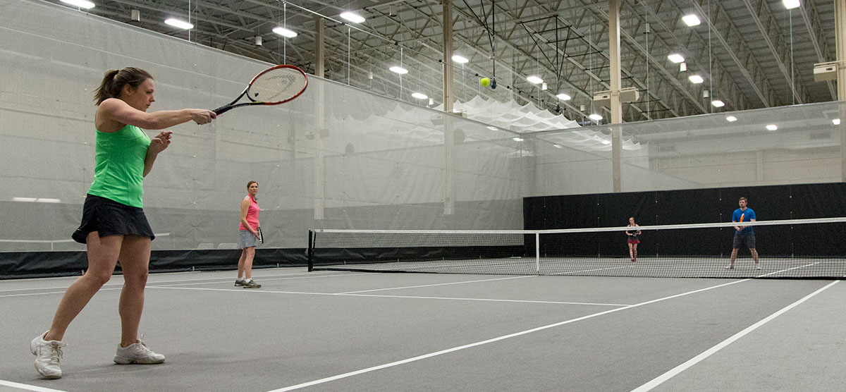 Player serving a tennis ball to the opposing team in the fieldhouse