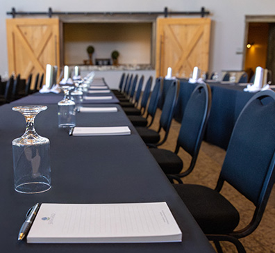 Long black table set up for a meeting with glasses and note pads