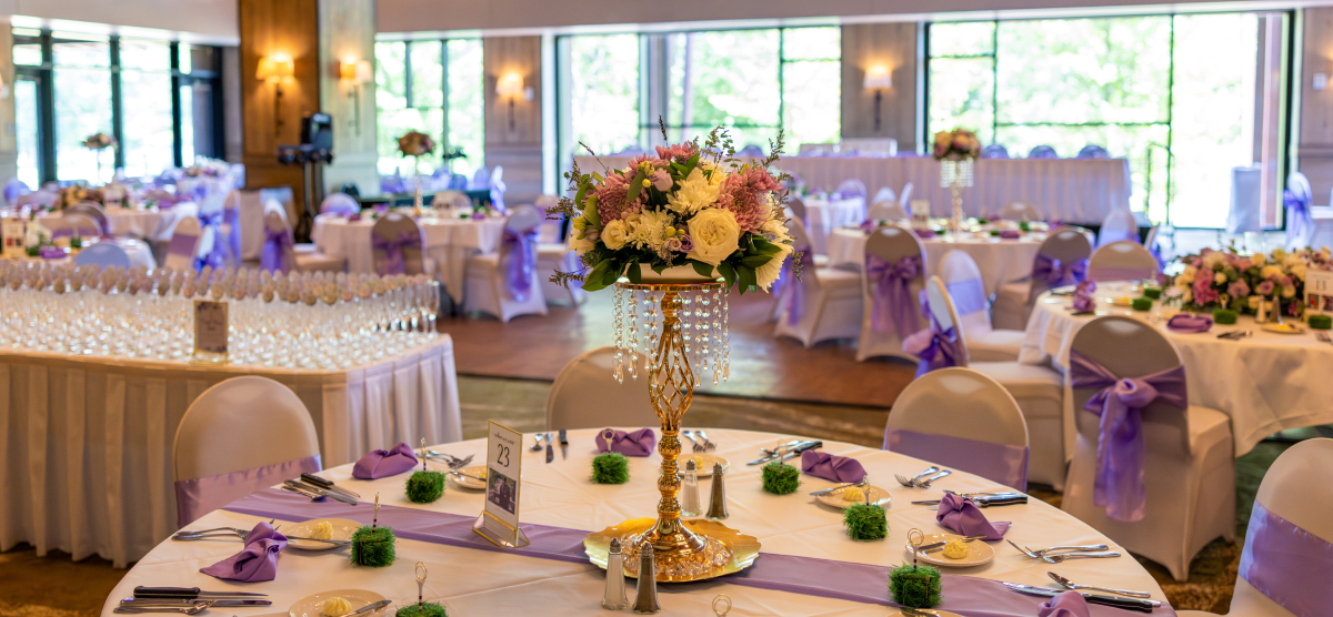 Event room with round tables set with white linens, purple accents, floral centerpieces, and champagne flutes.