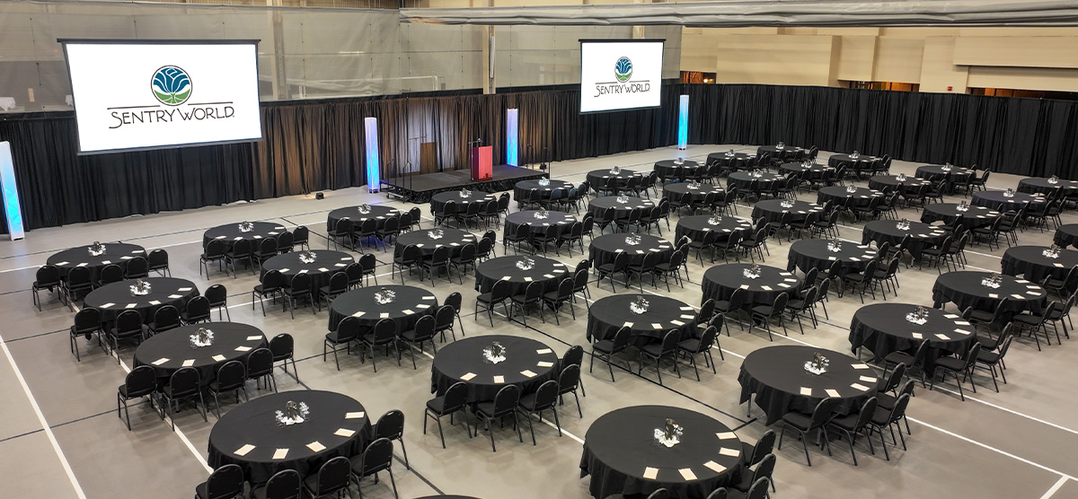 Aerial view of round tables and a projector screen set for an event in the fieldhouse at SentryWorld