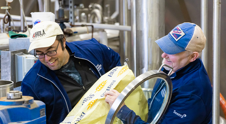 Two people putting beer ingredients in to make beer