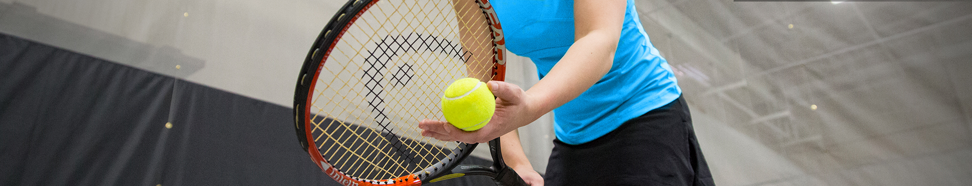 Player holding a tennis racket and ball in the fieldhouse at SentryWorld