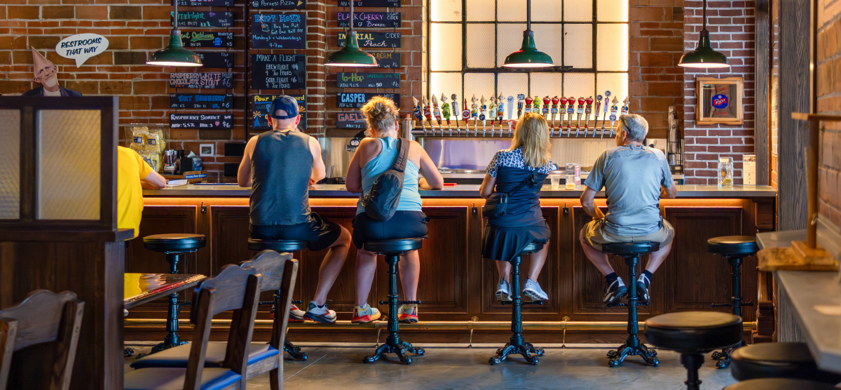 People sitting at a bar with beer taps and a brick wall in a pub.