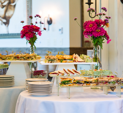 Buffet food next to plates and a vase of flowers