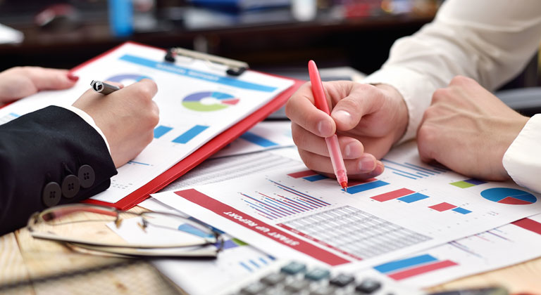 Two people reviewing paper graphs and reports