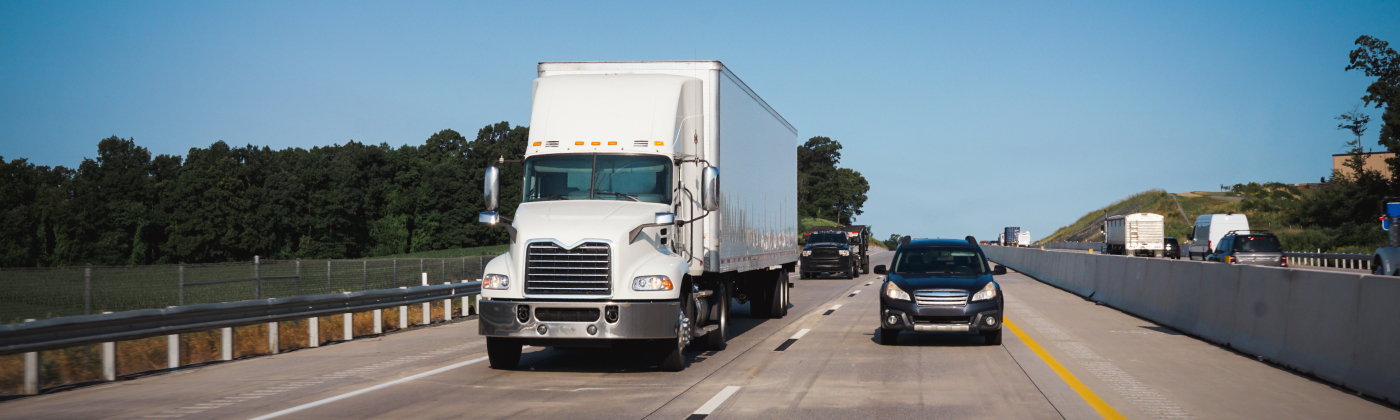 White semi-truck and cars driving on a highway under a clear blue sky.