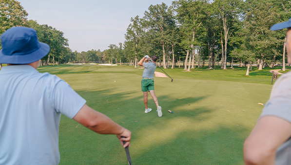 Golfer teeing off while two friends watch. 