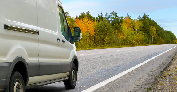 White delivery van parked on a road alongside autumn trees.