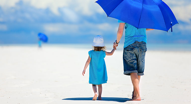 Child and parent walking on beach under umbrella