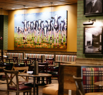 image-card-contact-pjs-396x364 PJ's restaurant interior with tables, booths, and a large painting of cows on the wall.