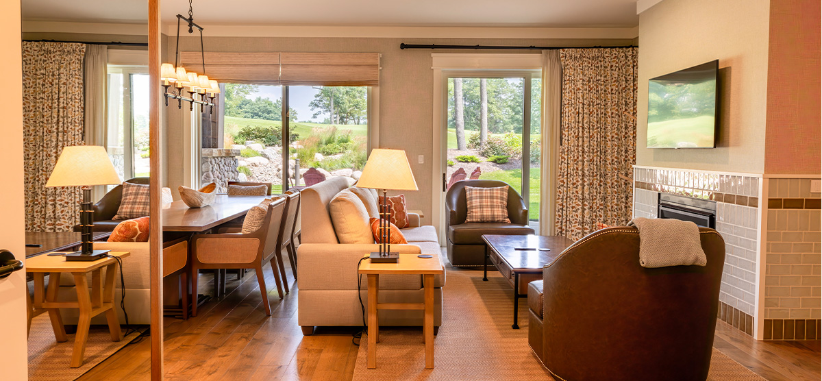 carousel-suite-golf-view-king-queen-6-1200x556 Suite parlor room with a dining room table and seating area.