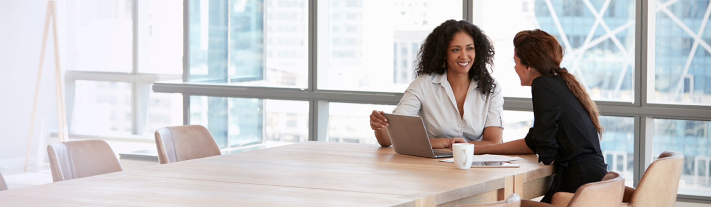 Two women in meeting smiling with laptop on table