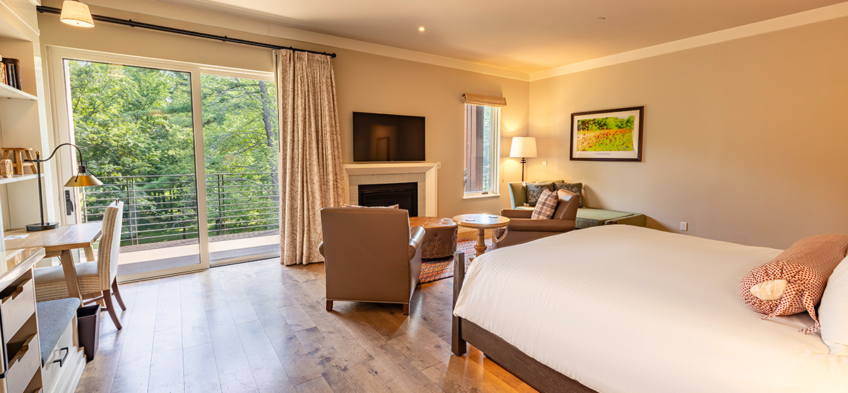 carousel-golf-view-executive-level-luxury-junior-suite-2-1200x556 King bed with seating area in front of a fireplace and patio door facing the golf course.