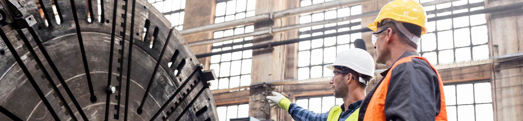 Two men in safety vests reviewing equipment on a manufacturing floor.