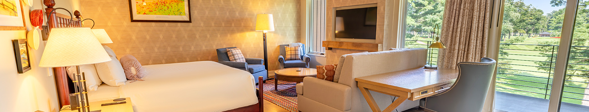 hero-lodging-rooms-1900x364 Hotel room with one king sized bed and seating area in front of fireplace.