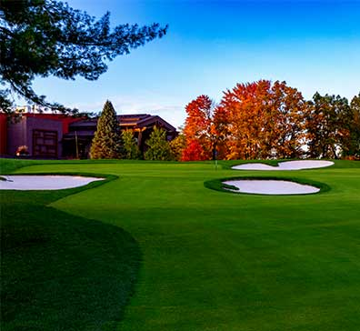 Putting green on the SentryWorld golf course next to sand traps and trees changing color in the fall