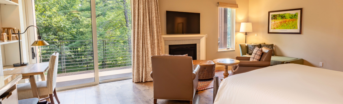 Hotel room with a bed, chairs in front of a fireplace, a desk, and a patio window with balcony.