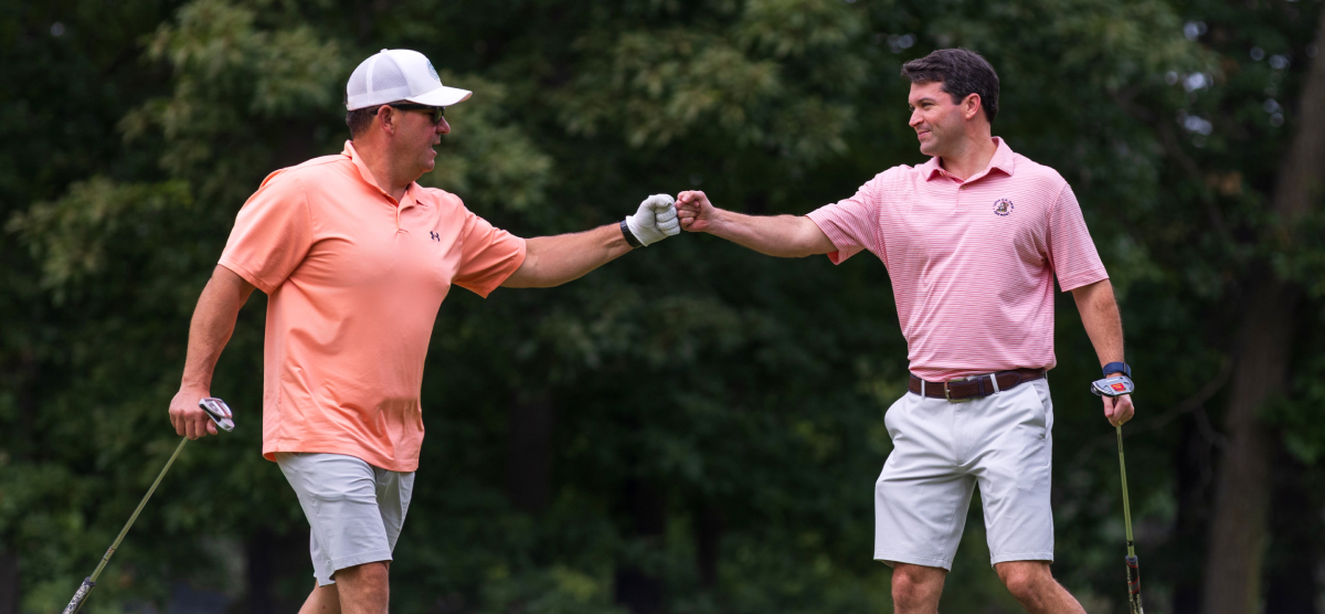 carousel-corporate-event-team-building-2-1200x556 Two golf players fist bump at SentryWorld golf course.