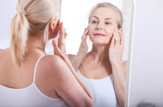 woman looking at skin in the mirror