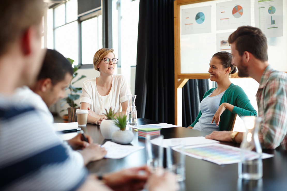 A group of people sitting together around a table and having a discussion. 