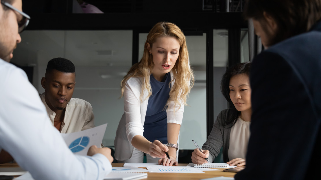 A group of people sitting around a table looking over documents together in a meeting. 