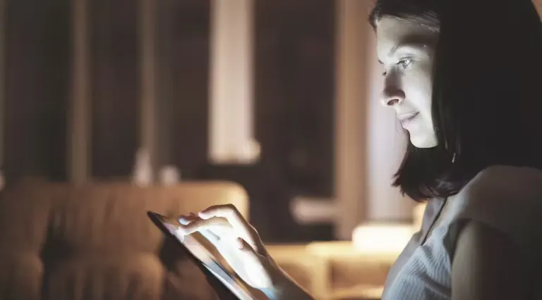 Woman sat in the dark in a living room looking at an iPad 