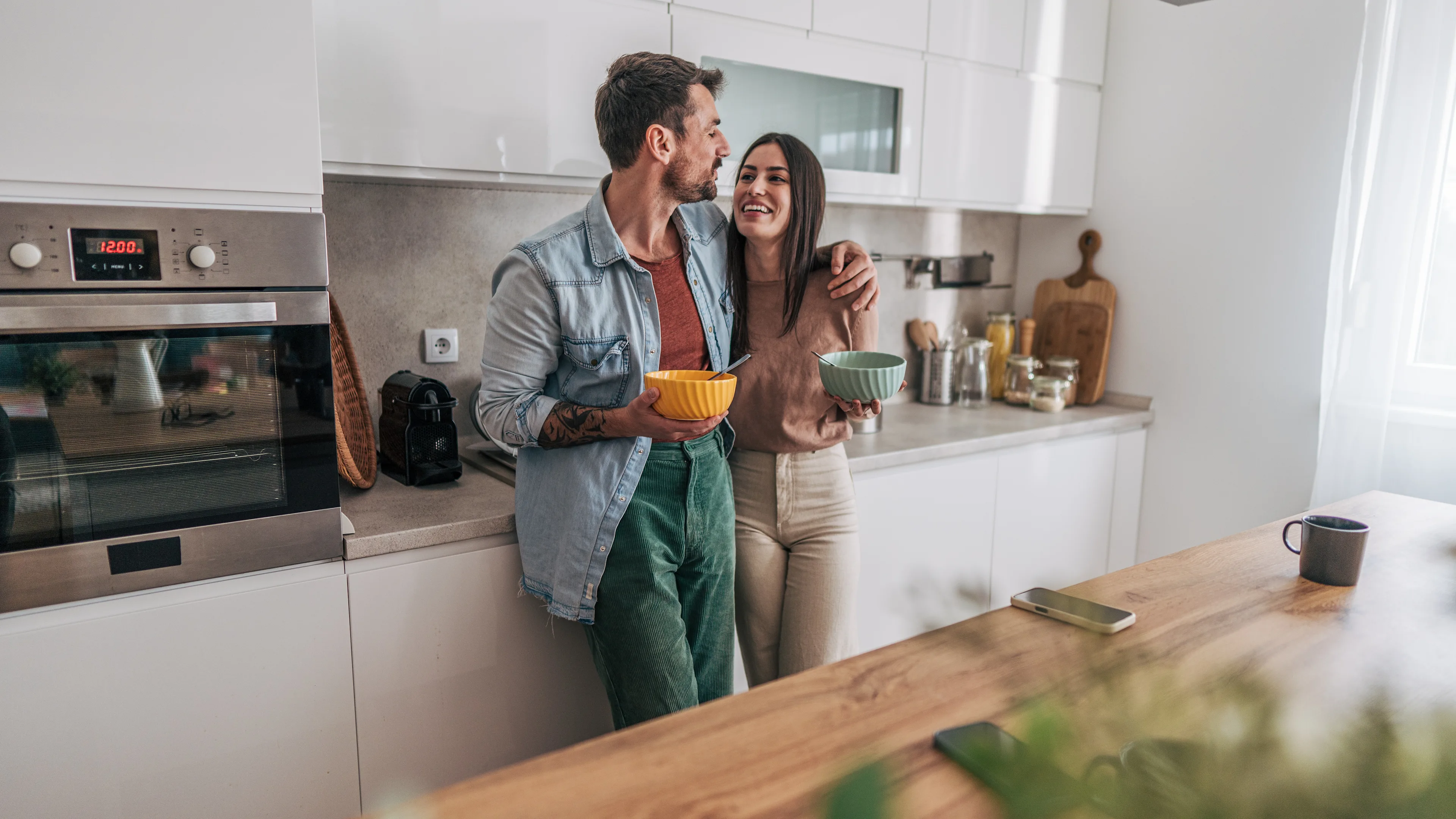 A couple in the kitchen of a house eating breakfast.
