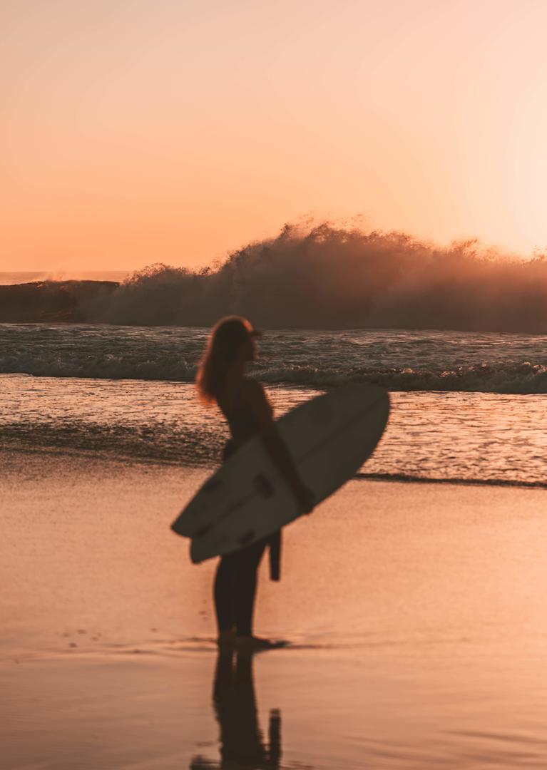Girl standing on the beach with surfboard during Sunset