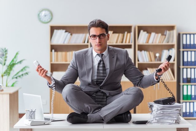 Business man sits on desk meditating with two work phones