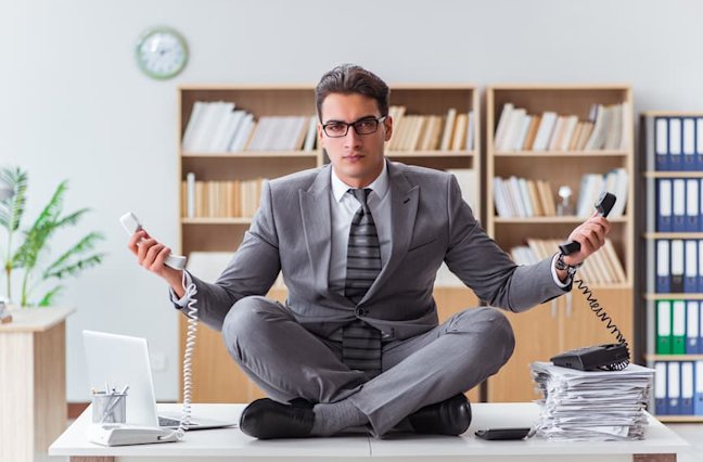 Business man sits on desk meditating with two work phones