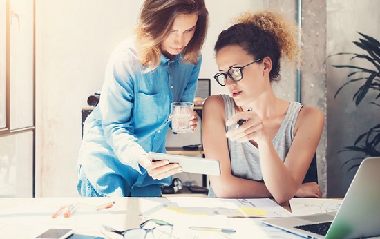 portrait of beautiful and cheerful young woman telephone operator with headset working on desktop computer in row in customer service call support helpline business center with co-worker in background
