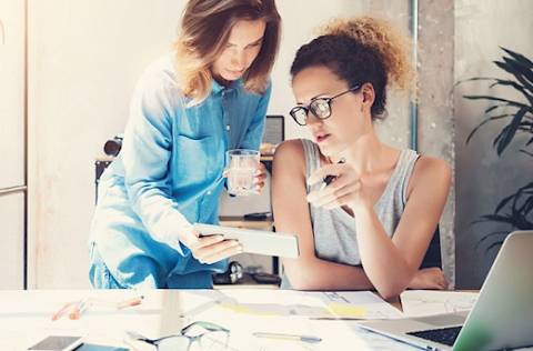 portrait of beautiful and cheerful young woman telephone operator with headset working on desktop computer in row in customer service call support helpline business center with co-worker in background
