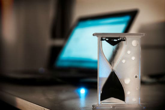 Hourglass sand running out, blurred out laptop in background